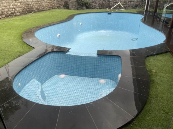 Freeform fully tiled luxury pool with pale blue water, light mosaic tiling and dark curved coping