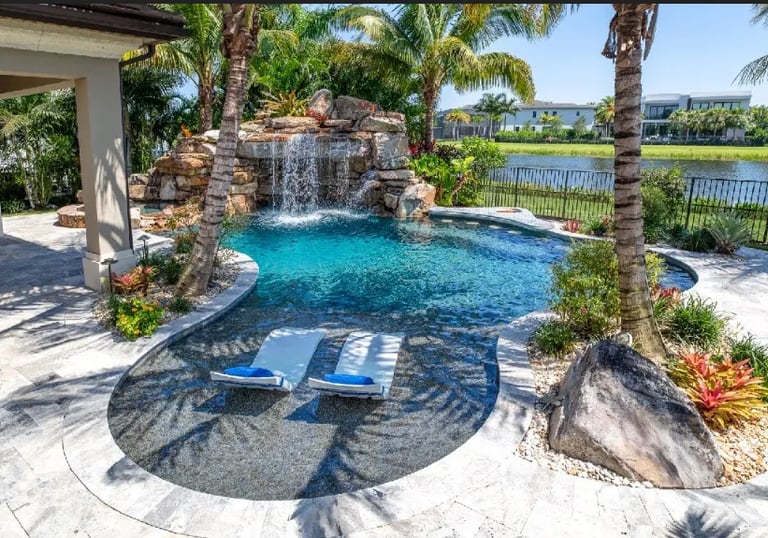 Freeform lagoon pool with aqua water, natural rock waterfall and light pebble interior creating a tr