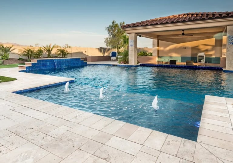 Geometric pool with dark blue water and light stone tiling, featuring raised spa and deck jets.