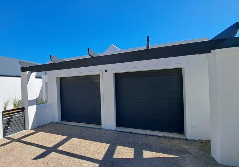 Modern white double garage with dark grey sectional doors and a black wooden pergola.