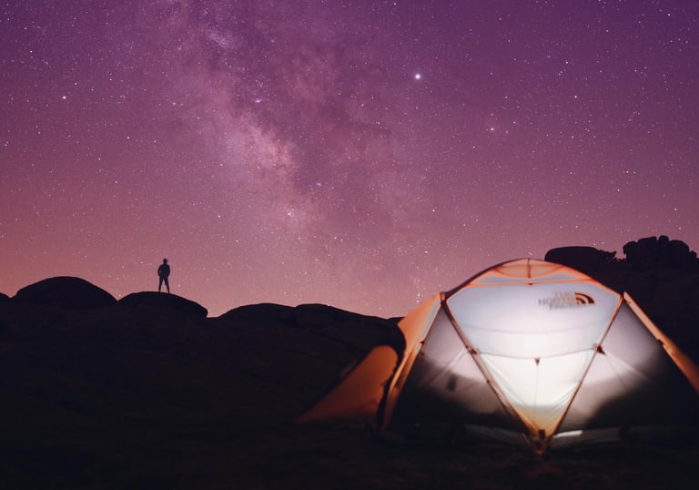 a person standing in front of a tent with a bright purple starry night sky