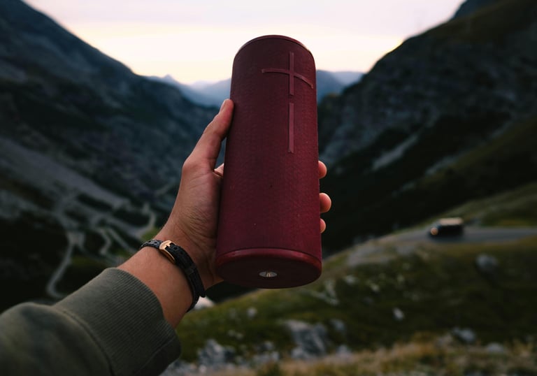 a person holding a red bluetooth speaker in their hand overlooking a mountain