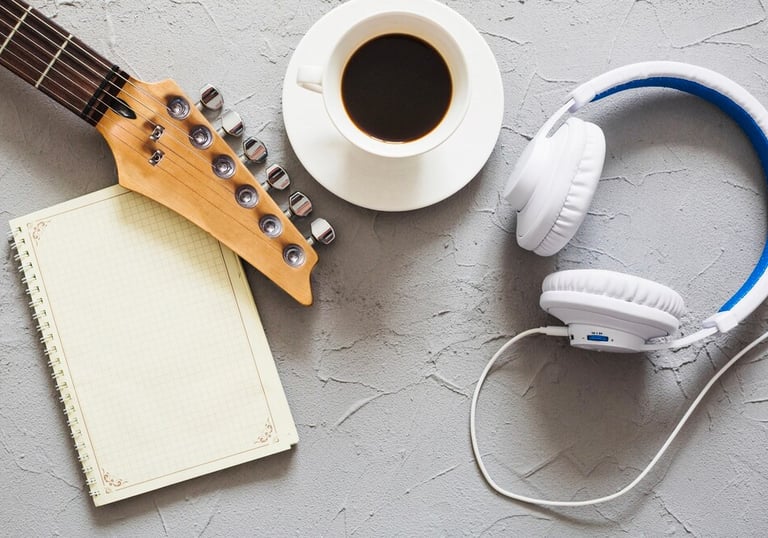 Guitare, tasse de café, casque audio, et cahier posés sur une table.