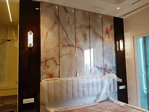 Luxury master bedroom featuring a polished onyx marble wall panel with modern gold sconces.