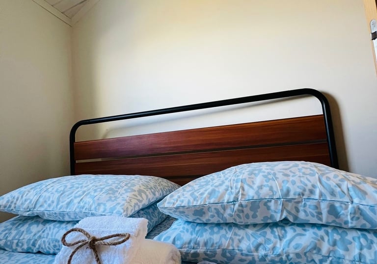 Cozy bedroom interior with blue floral bedding and fresh white towels tied with twine on a wood and metal bed frame.