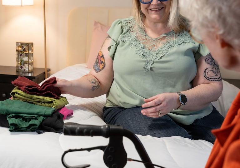 In-home caregiver assisting a senior woman with laundry and folding clothes in a bedroom.