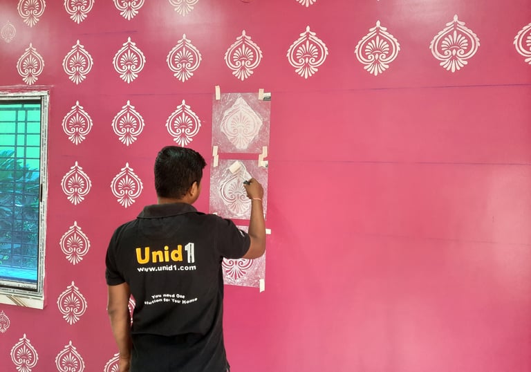 Professional painter applying a white damask stencil pattern on a pink interior accent wall.