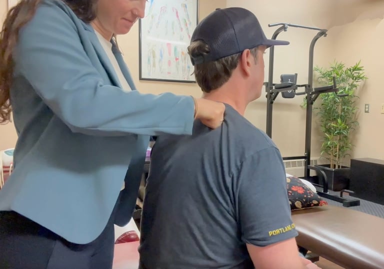Chiropractor performing deep tissue work on seated patient's shoulder in treatment room. 