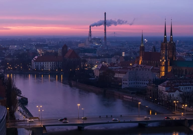 Wroclaw city skyline at twilight with the Odra River, illuminated bridges, and the cathedral under a purple sunset.