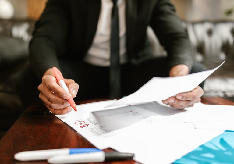 A man in a suite at his desk, writing on financial papers with a red marker