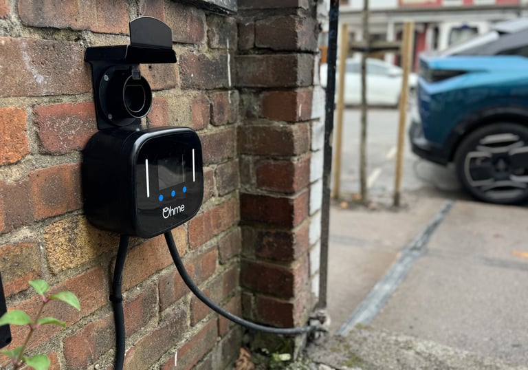 Black Ohme smart electric vehicle charger mounted on a brick wall for residential EV charging.