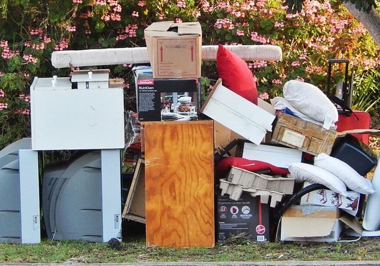 junk on a curb in front of a house consisting of a piece of furniture, garbage bags, pillows, TVs