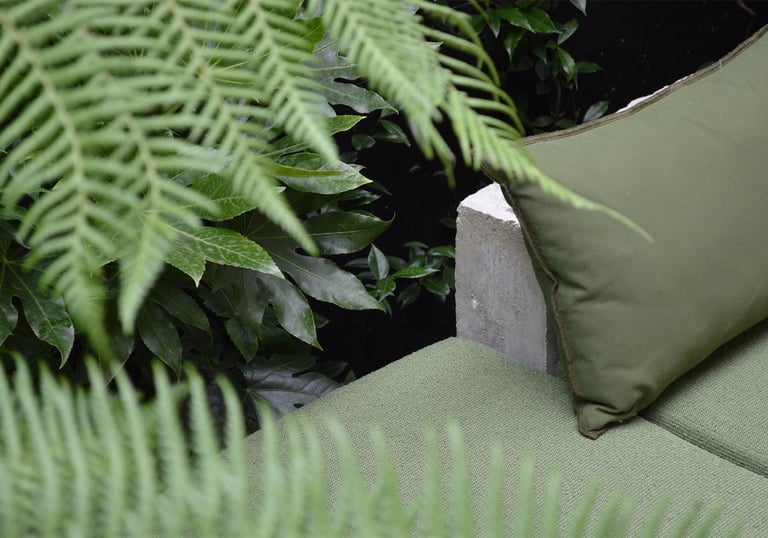Green outdoor sofa cushions and pillows surrounded by lush garden fern leaves.