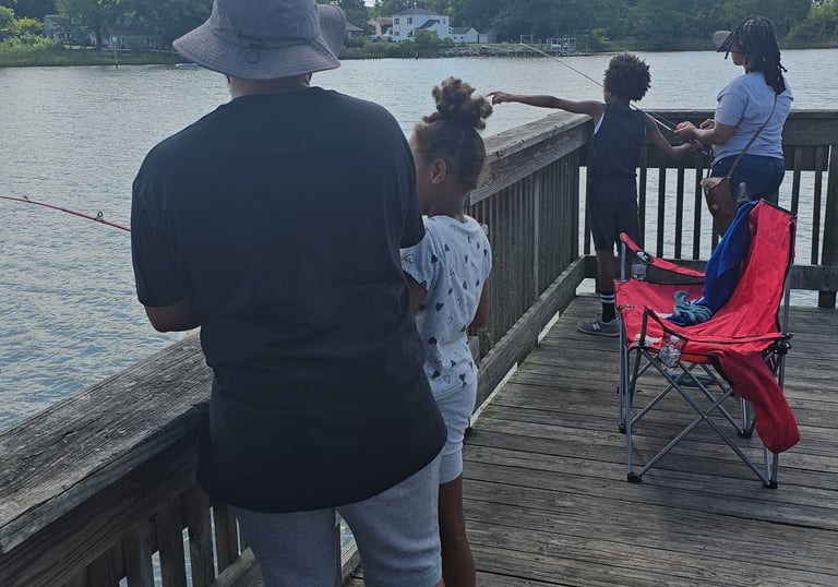 A family fishing together from a wooden pier on a sunny day with blue skies and fluffy clouds.