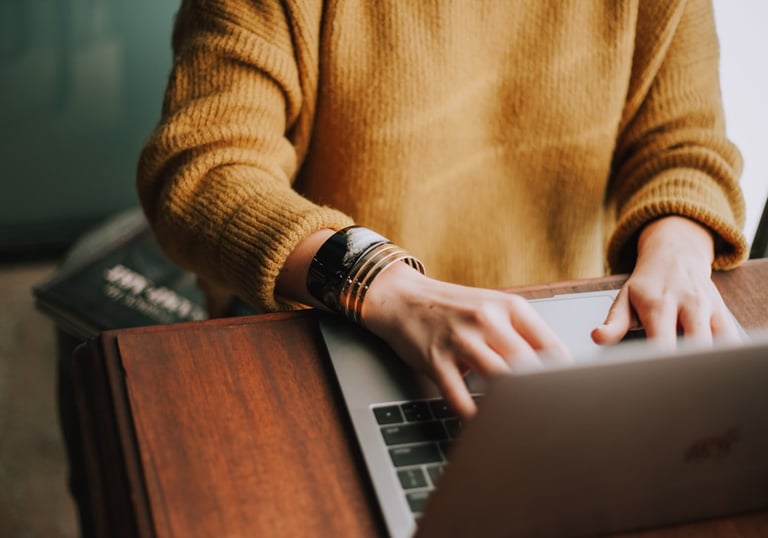 woman in yellow sweater typing on a laptop