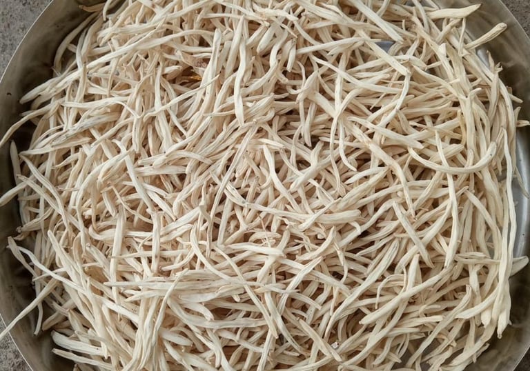 A close-up of fresh safed musli roots on a wooden surface.