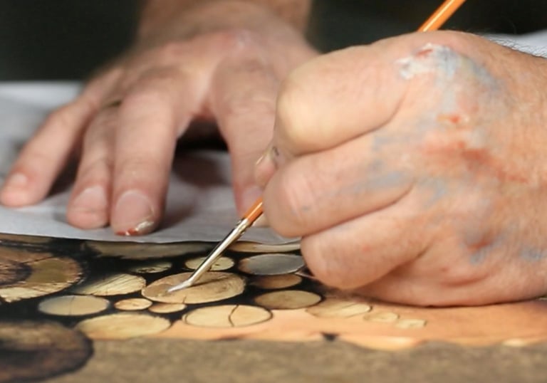 Artist painting intricate wood grain details on a canvas with a fine tip paintbrush.