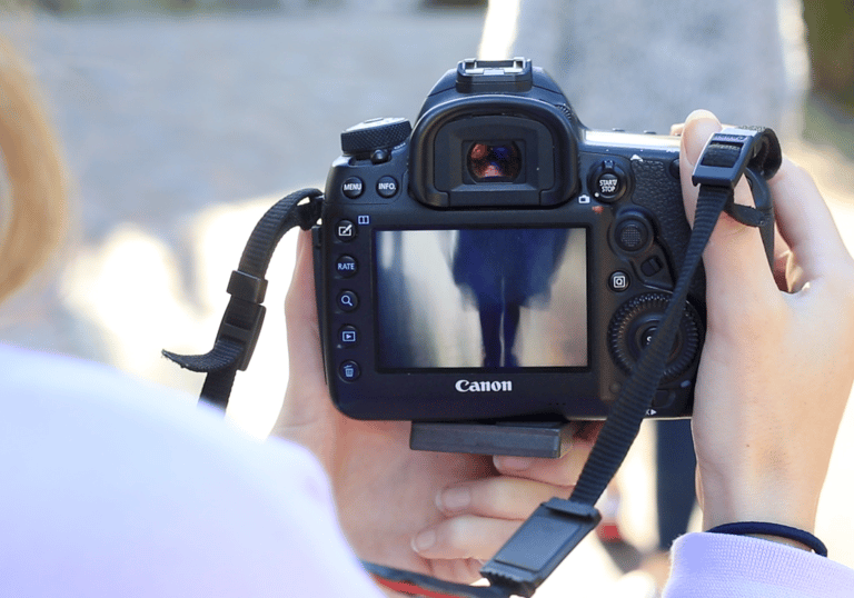 Photographer holding a Canon DSLR camera while reviewing photos on the LCD screen outdoors.