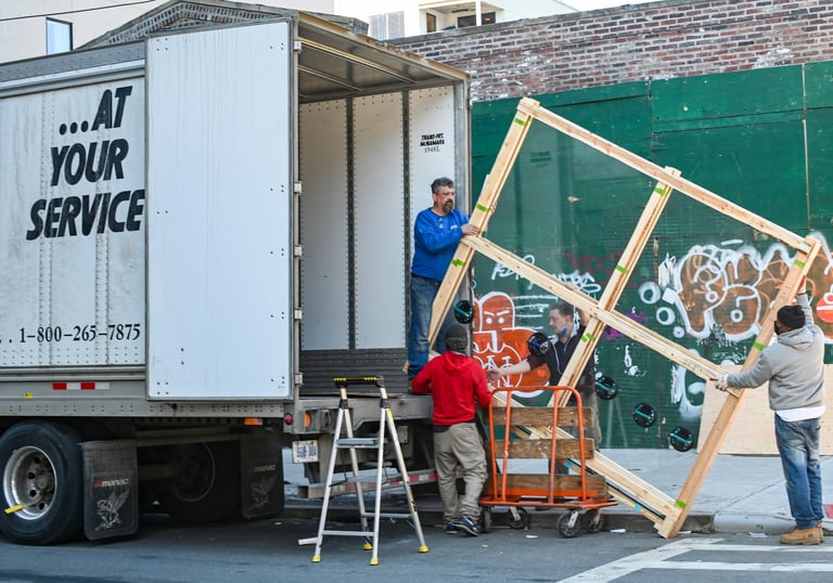 Four people lifting a large window out of a moving truck