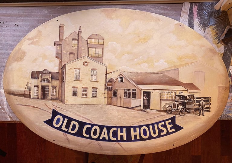 Oval pub sign with painted brewery buildings and name in blue ribbon.