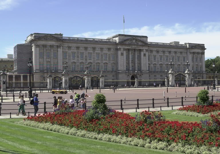 Exterior view of Buckingham Palace with vibrant flower beds in the foreground. 