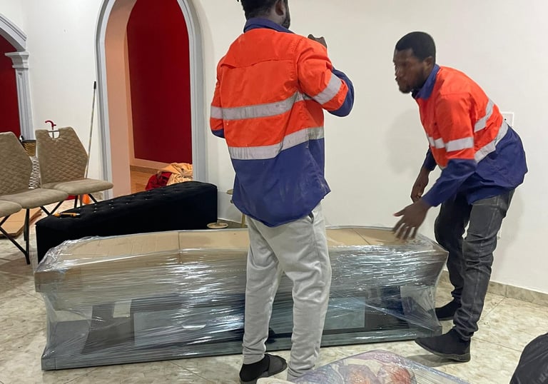 Two professional movers in orange high-visibility jackets with reflective strips collaborate to lift