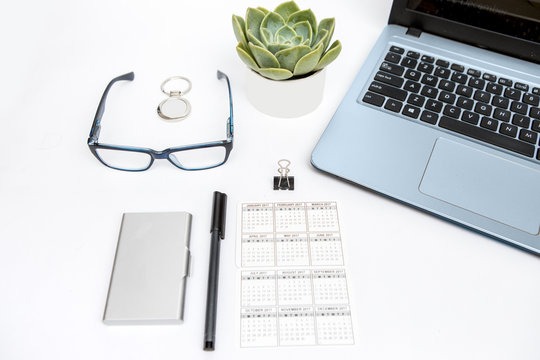 Minimal workspace with laptop, calendar, eyeglasses, and plant