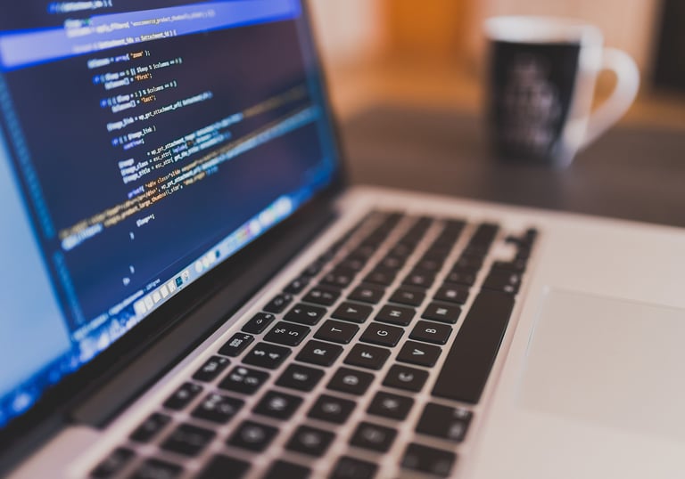 A tela de um laptop exibindo o código de um software de desenvolvimento web, com uma xícara de café