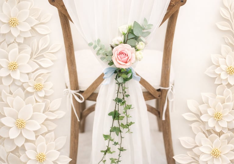 Elegant wooden wedding chair with white tulle drape and a pink rose floral arrangement.