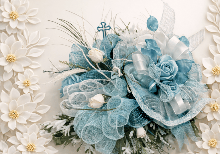Blue and white artificial flower arrangement with deco mesh ribbons and a small blue cross.