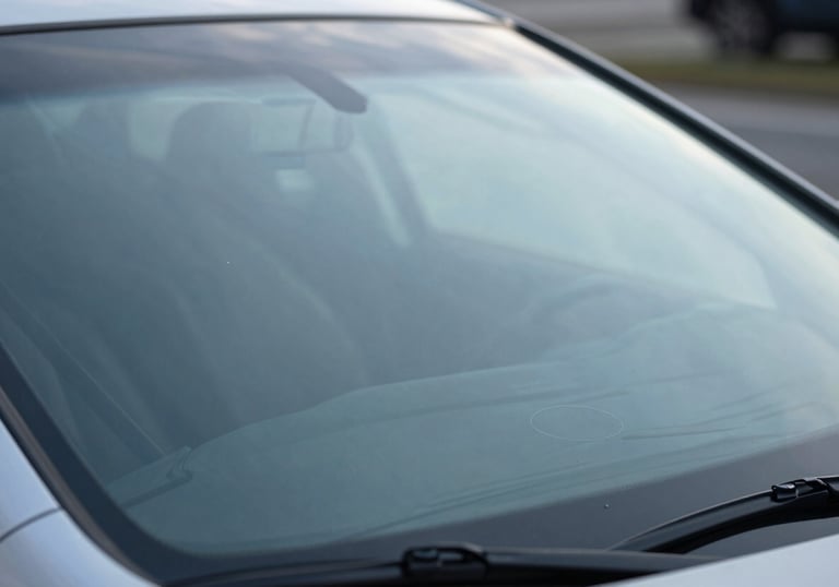 Macro photography of a new, pristine car windshield showing a subtle manufacturer's stamp of quality, reflecting a soft light blue sky.