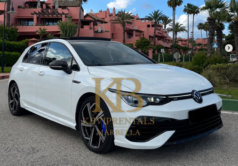 White Volkswagen Golf R parked in front of pink Mediterranean villas in Marbella, Spain.