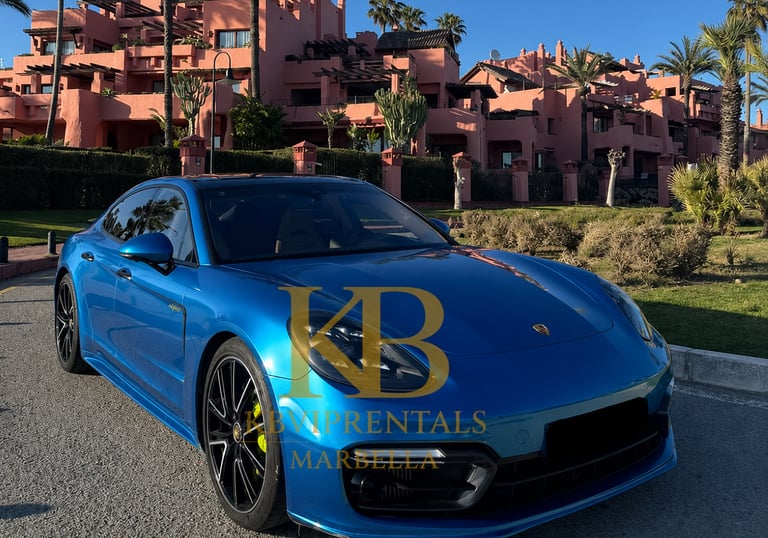 Blue Porsche Panamera luxury rental car parked in front of pink Mediterranean villas in Marbella.
