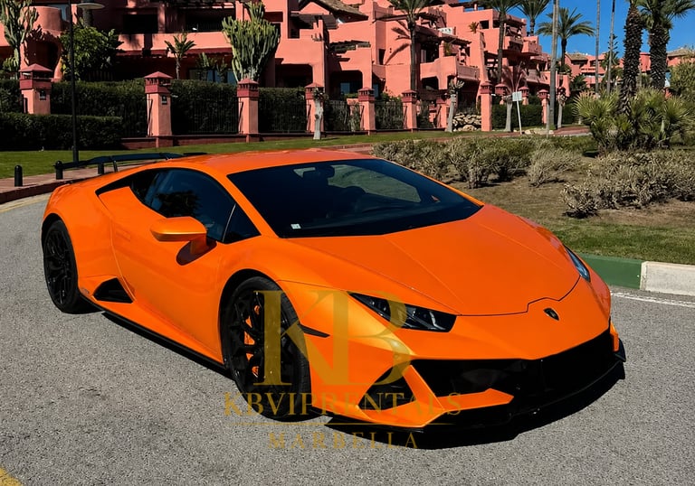 Orange Lamborghini Huracan luxury supercar parked in front of pink Mediterranean villas in Marbella.