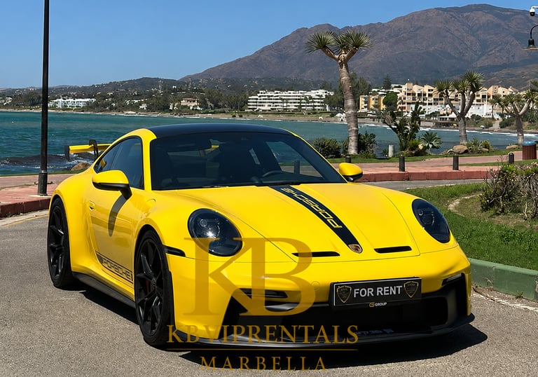 Yellow Porsche 911 GT3 luxury car rental parked on the Marbella coast with mountain views.