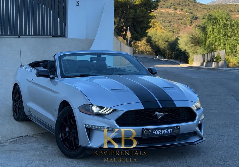 Silver Ford Mustang convertible with racing stripes parked on a scenic Marbella road for luxury car rental.