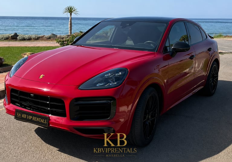 Red Porsche Cayenne Coupe luxury car rental parked by the ocean in Marbella.