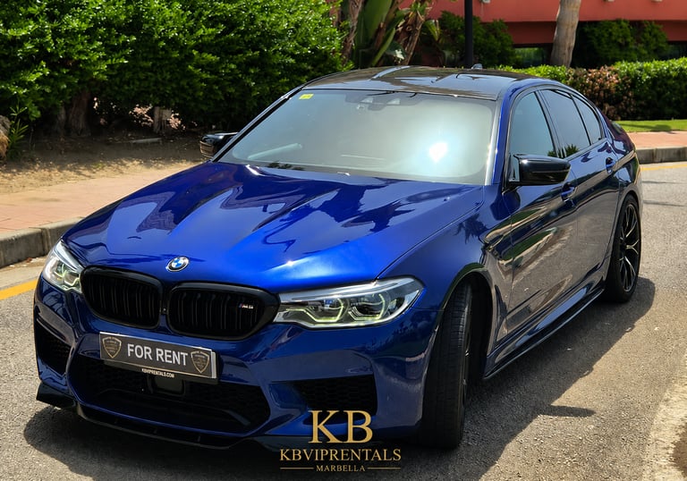 Luxury blue BMW M5 sedan for rent parked on a sunny street in Marbella, Spain.
