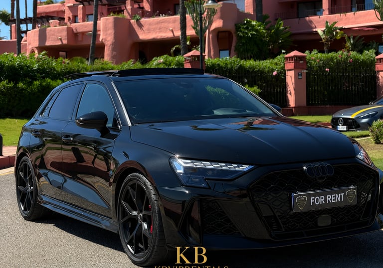 Black Audi RS3 hatchback rental parked in front of a luxury pink resort in Marbella.