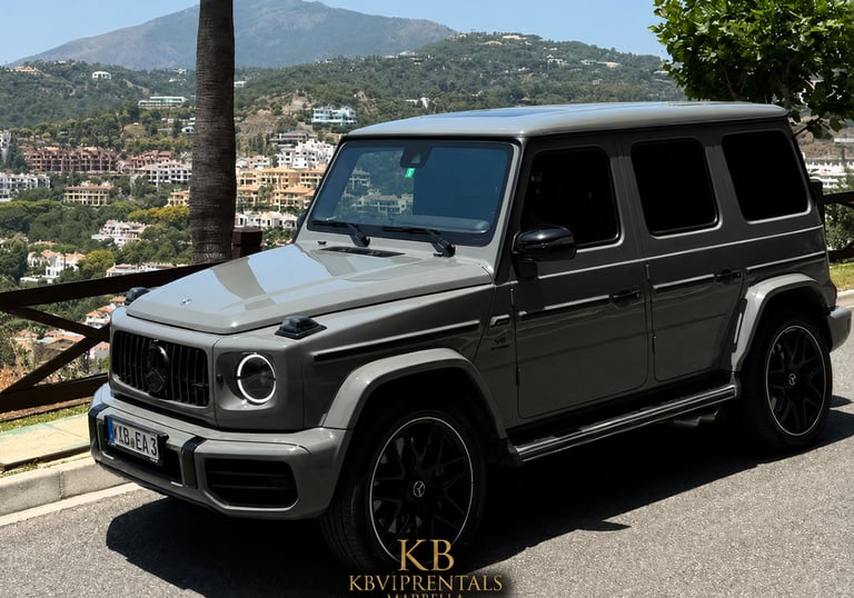 A luxury grey Mercedes-Benz G-Wagon parked on a scenic Marbella hillside overlooking the mountains.