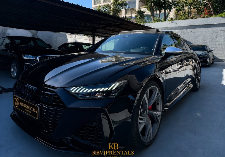 Black Audi RS7 luxury car rental parked in a Marbella showroom with LED headlights on.