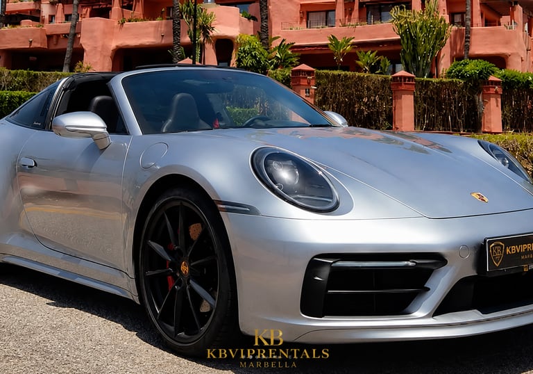 Silver Porsche 911 Targa luxury rental car parked in front of a Mediterranean resort in Marbella.