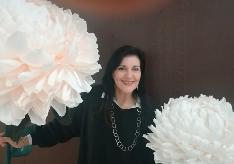 Clara Mennella sorride tra grandi fiori scenografici durante un evento legato al mondo del food & wine.