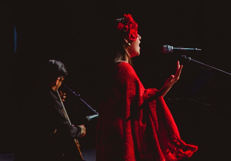 A woman in a red dress with flower hairpiece singing into a microphone during a live musical performance.