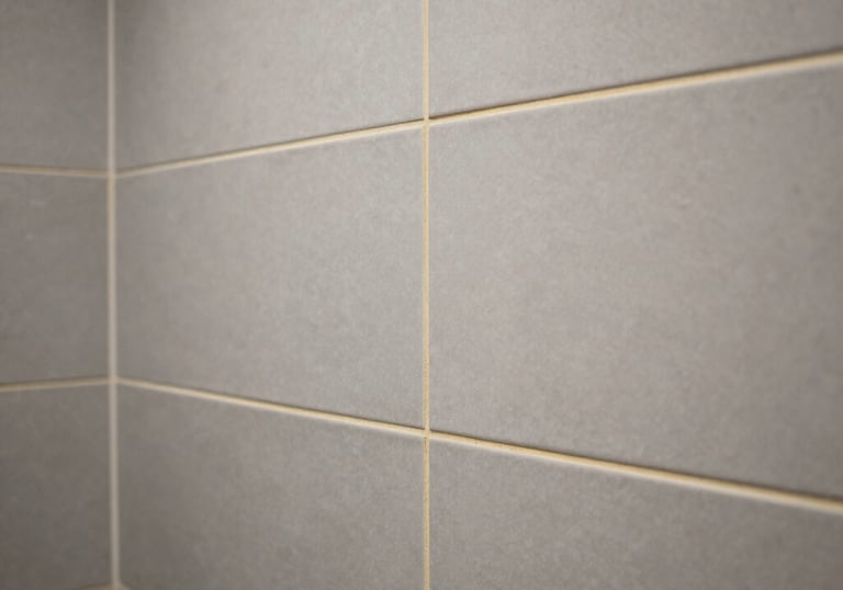 Detailed shot of a luxury bathroom tile installation, showcasing precise alignment and clean grouting lines, soft grey palette with gold accents.