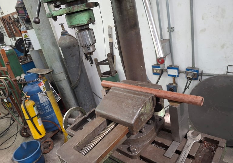 Una prensa de taladro sujetando un tubo de madera en un taller listo para perforarlo