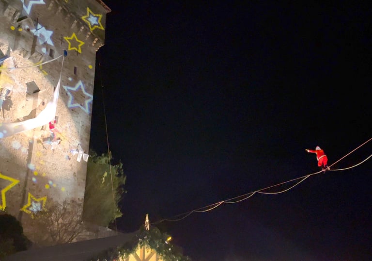 Le pere Noel marche en equilibre sur un fil en direction de mere noel suspendue a un tissu