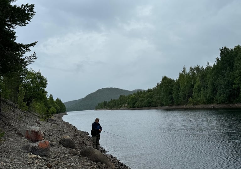 a man fishing on a rocky shore of a lake