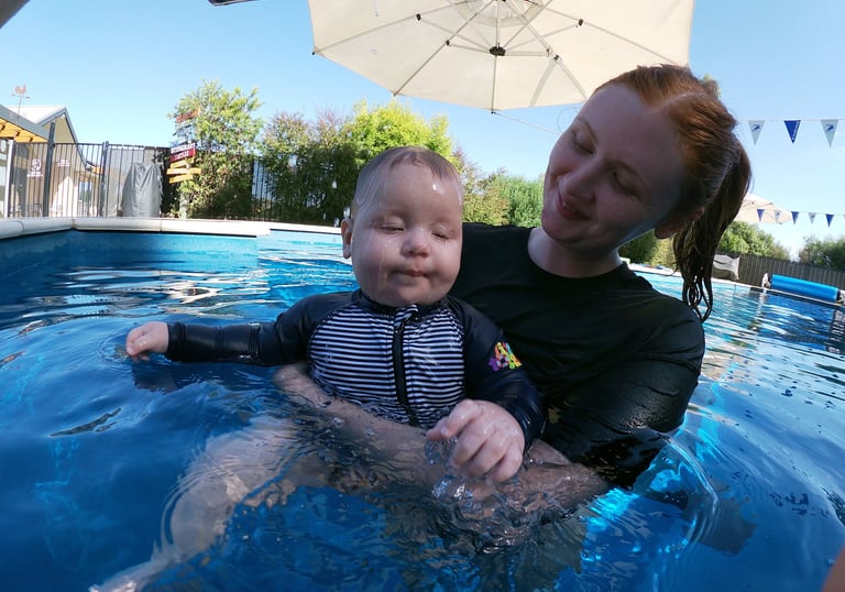 a woman in a swimsuit is holding a baby in a pool, preparing the baby for submersion