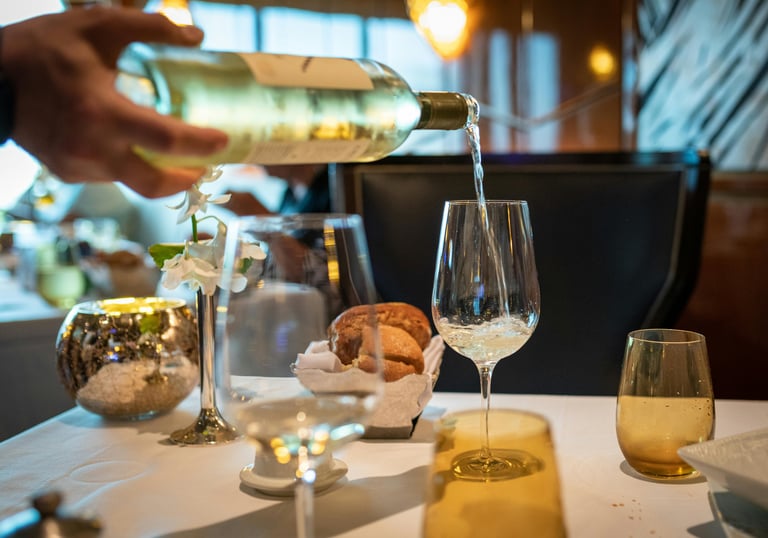 hand pour white wine and beautifully set dinner table